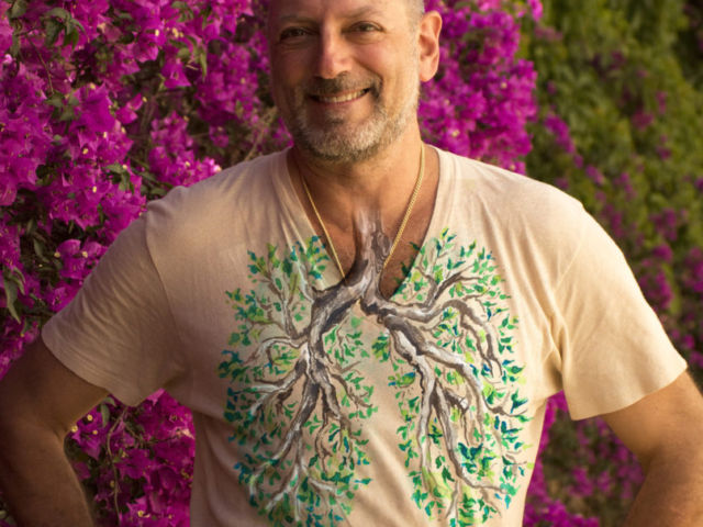 Leslie wearing a lung tree tee shirt in front of a beautiful magenta tree in Barcelona